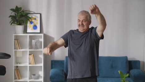 Un-Hombre-Gracioso-Con-Bigote-Está-Haciendo-Ejercicio-Físico-Por-La-Mañana-En-Casa-Levantando-Y-Bajando-Las-Manos-Retrato-Medio-En-El-Interior